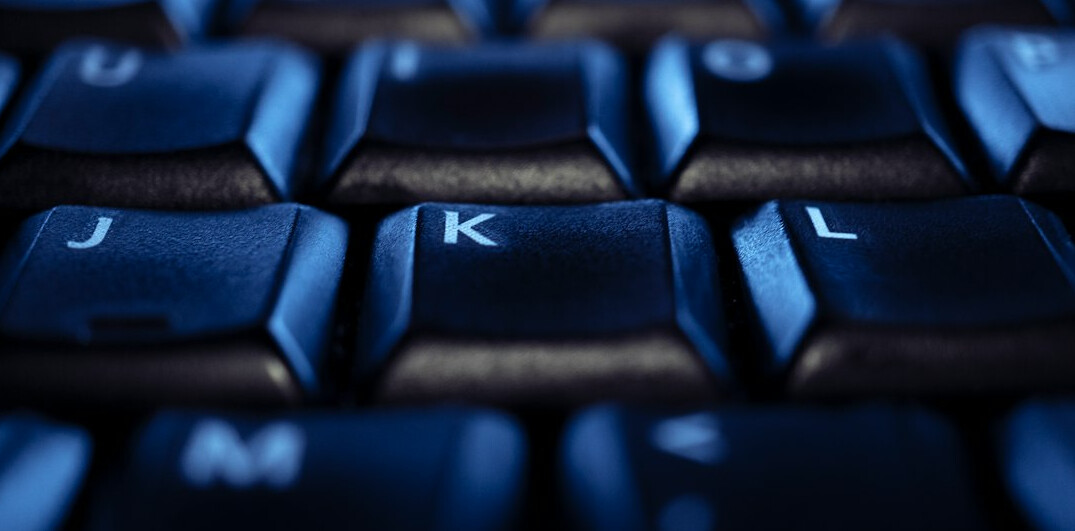 Close-up of hands typing on a laptop keyboard with code on screen